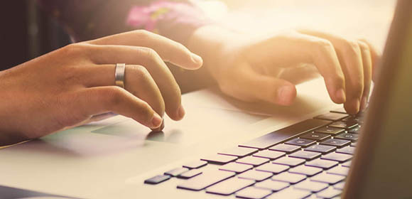 Pessoa digitando em um laptop, concentrada em sua tarefa, com as mãos sobre o teclado e a tela iluminada